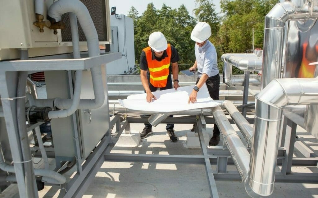 Zwei Ingenieure mit Plan neben Rohren auf Dach